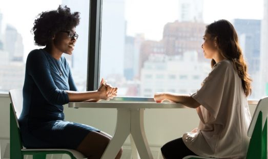 Two women have a conversation while sat around a small table
