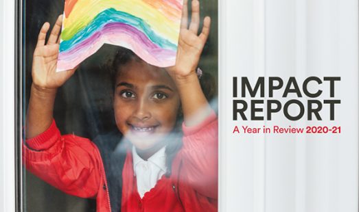 image of young girl holding up a rainbow picture against a window. Image used on the front cover of the Impact Report 202-21